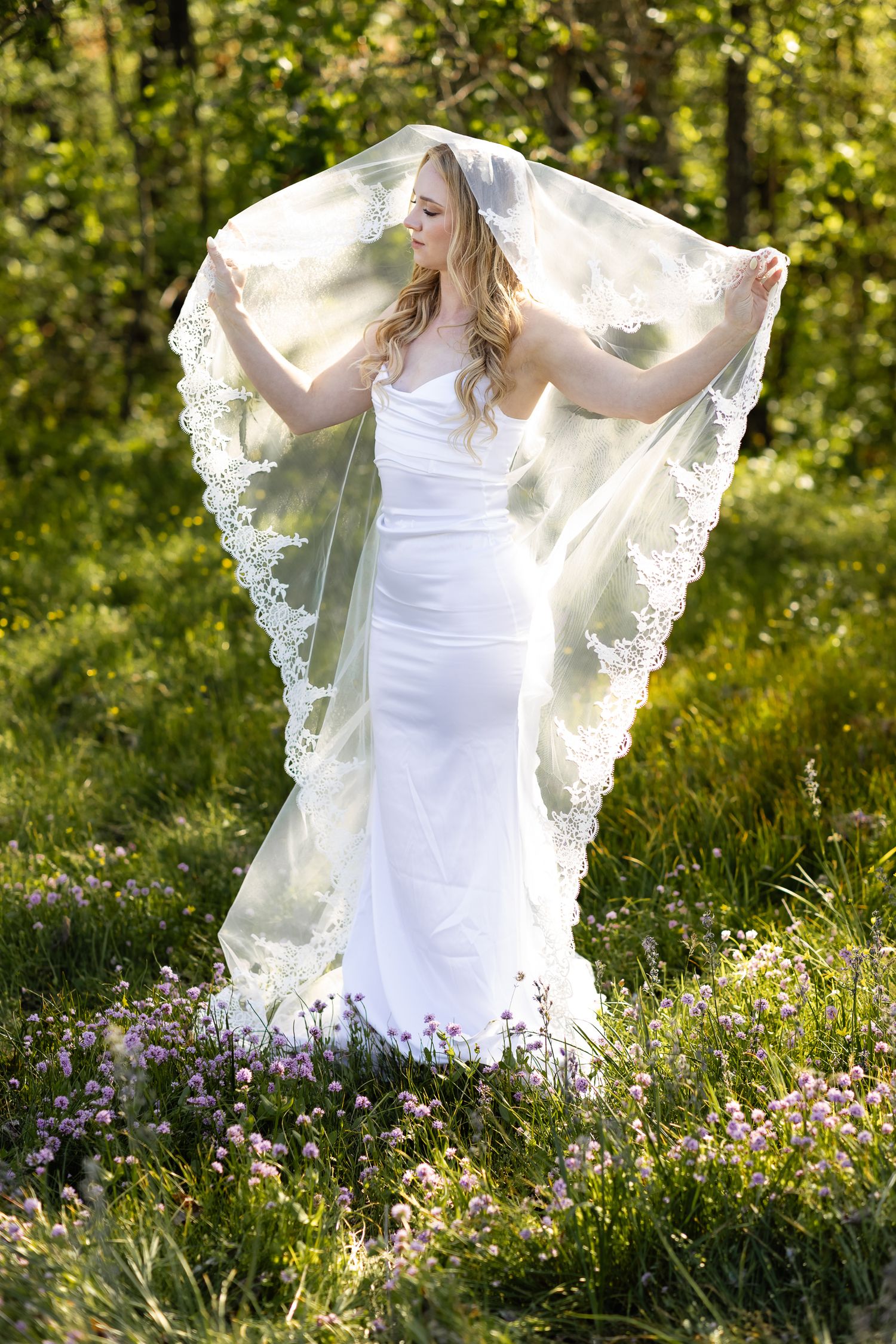 Bride poses in her mantilla wedding veil, in a meadow with small purple wildflowers in the Columbia River Gorge.