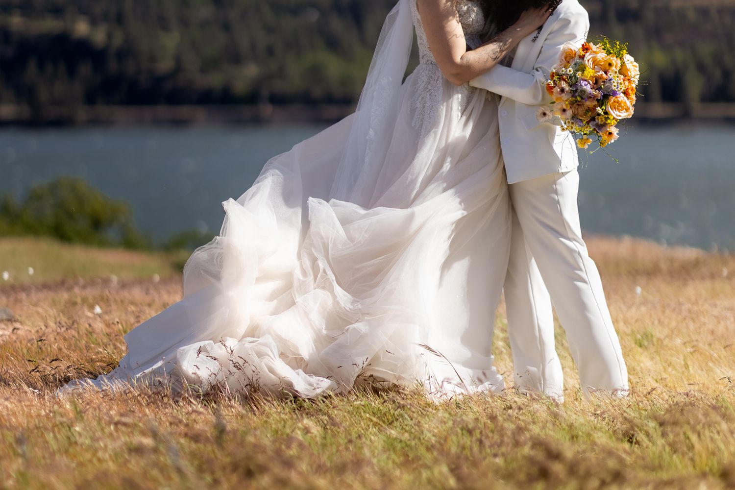 LGBTQ brides embrace on their windy elopement day in a field overlooking the Columbia River Gorge.