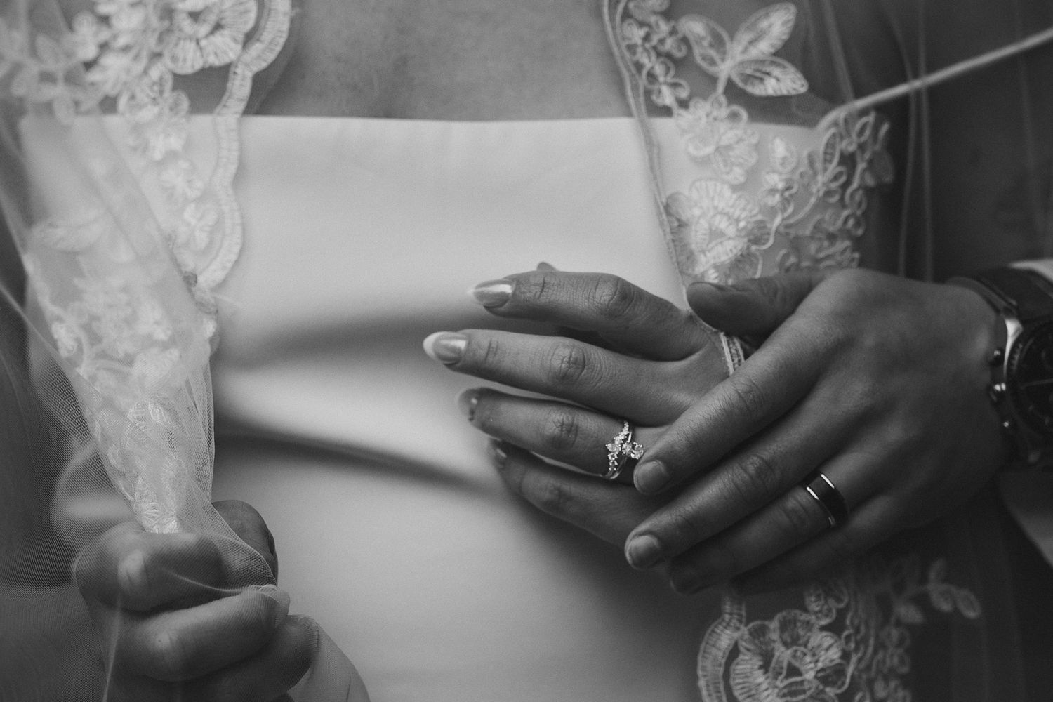 Editorial black and white edit of a bride and groom's hands with their wedding rings in sharp focus.
