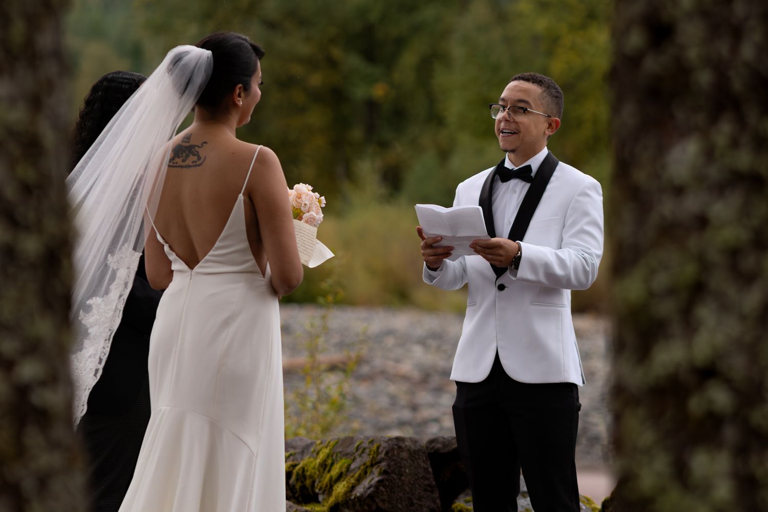 Jack reads his thoughtfully written vows to Yuri along the Nisqually River, seen from a perspective through trees in the foreground.