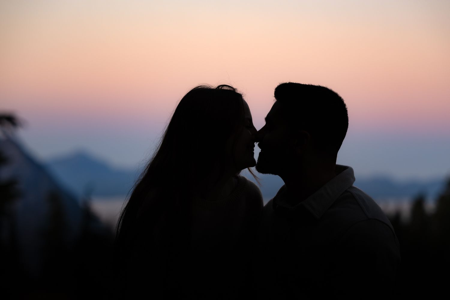 High-contrast outline of a couple moving in for a kiss in the mountains, with a dramatic cotton candy sunrise at Mount Rainier.
