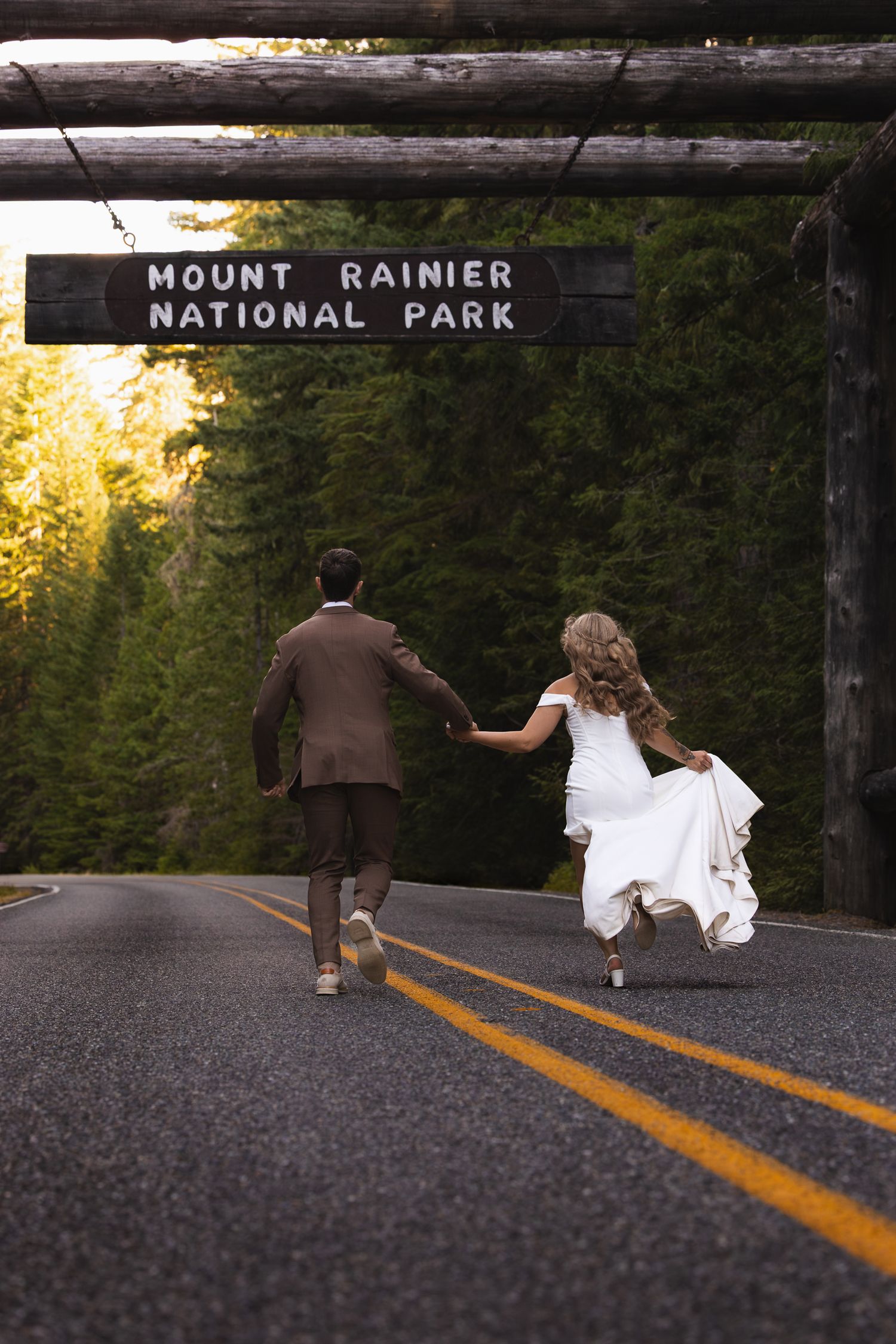 Moody contrasted edit of a bride and groom running under the Nisqually Mount Rainier park entrance sign during their elopement day.