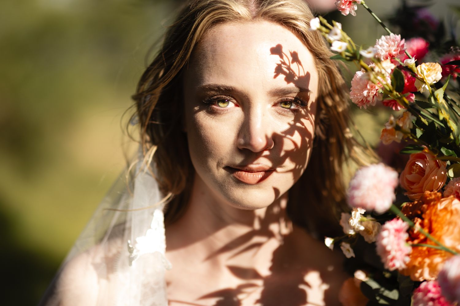 A bride wearing a veil looks into the camera on a sunny day in the Columbia River Gorge. She is painted with shadows from a flower arch.