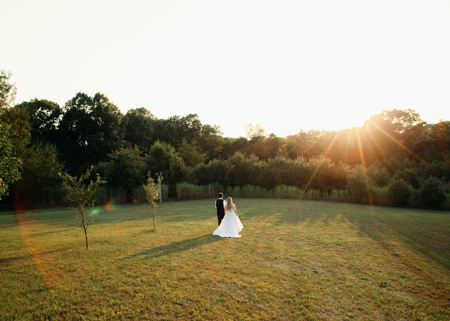 Wide-angle photo of a bride and groom running toward golden hour light at a Michigan wedding, photographed by Audrey Jo Photo.