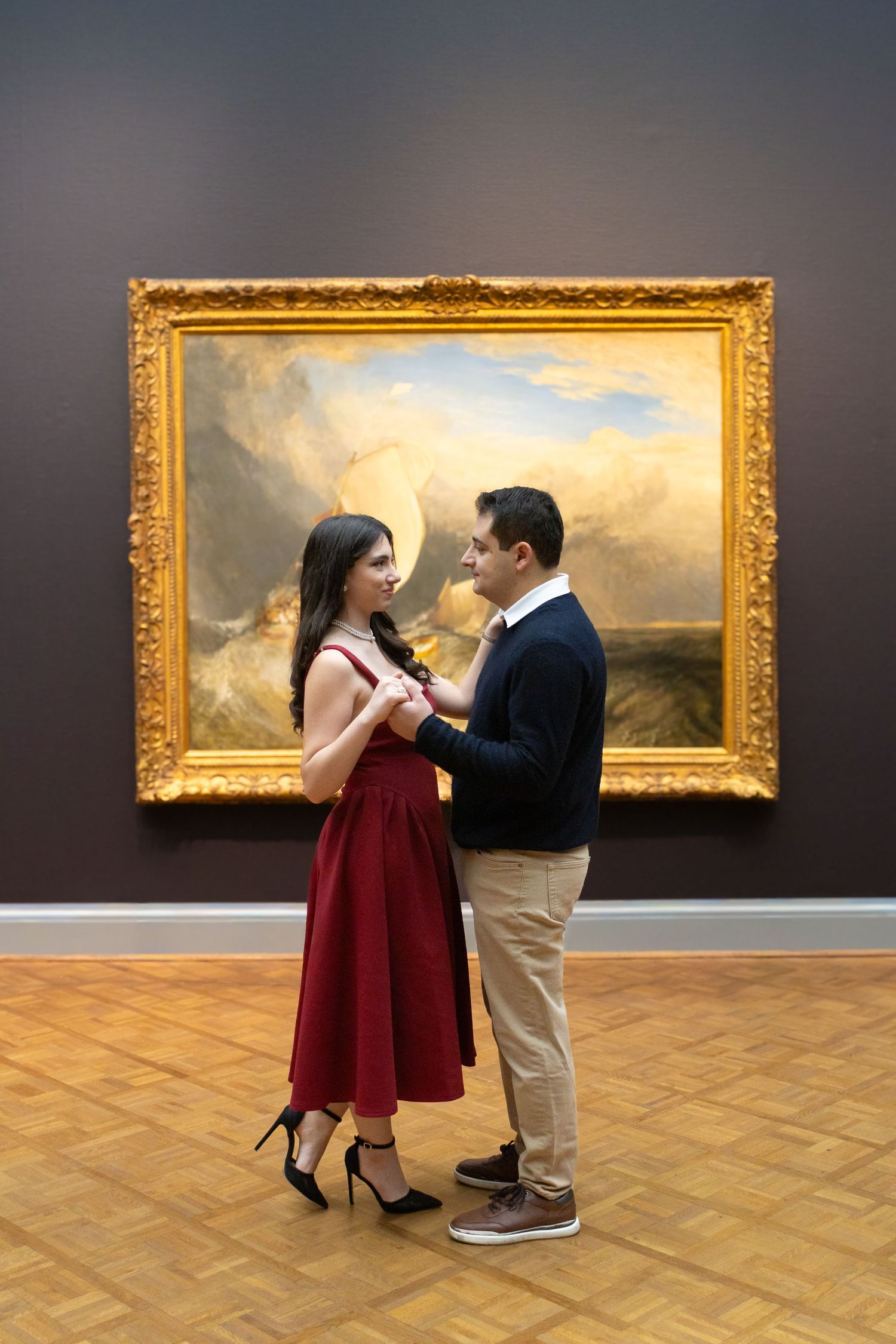 A couple shares a romantic moment in front of landscape paintings in an art gallery.
