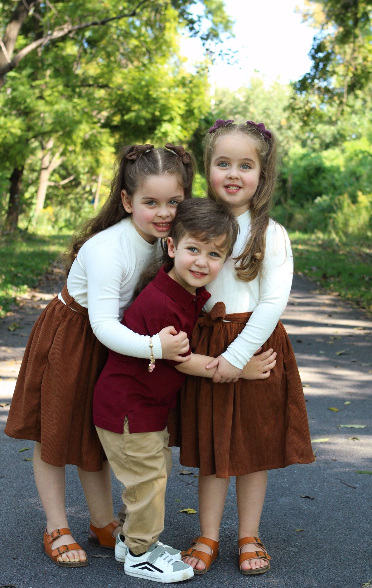 Two young children in brown and burgundy outfits playfully pose together on a path.