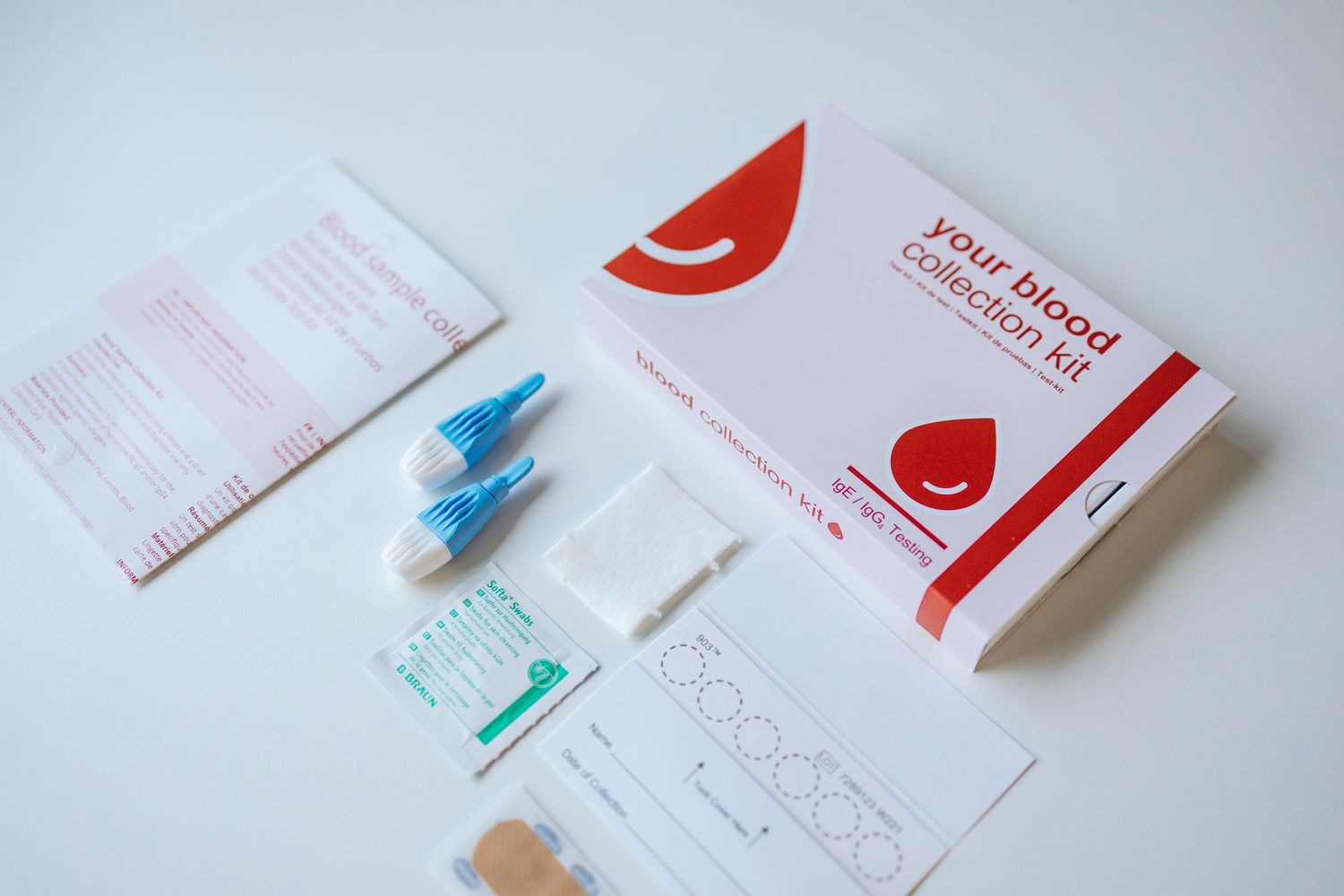 A blood testing kit with blue lancets, paperwork, and medical supplies spread on a white surface.