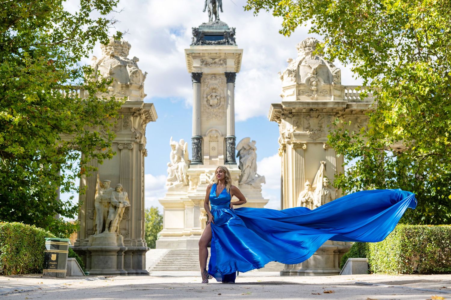 Bright blue fabric flowing gracefully in the breeze against ornate white stone architecture and lush green trees.