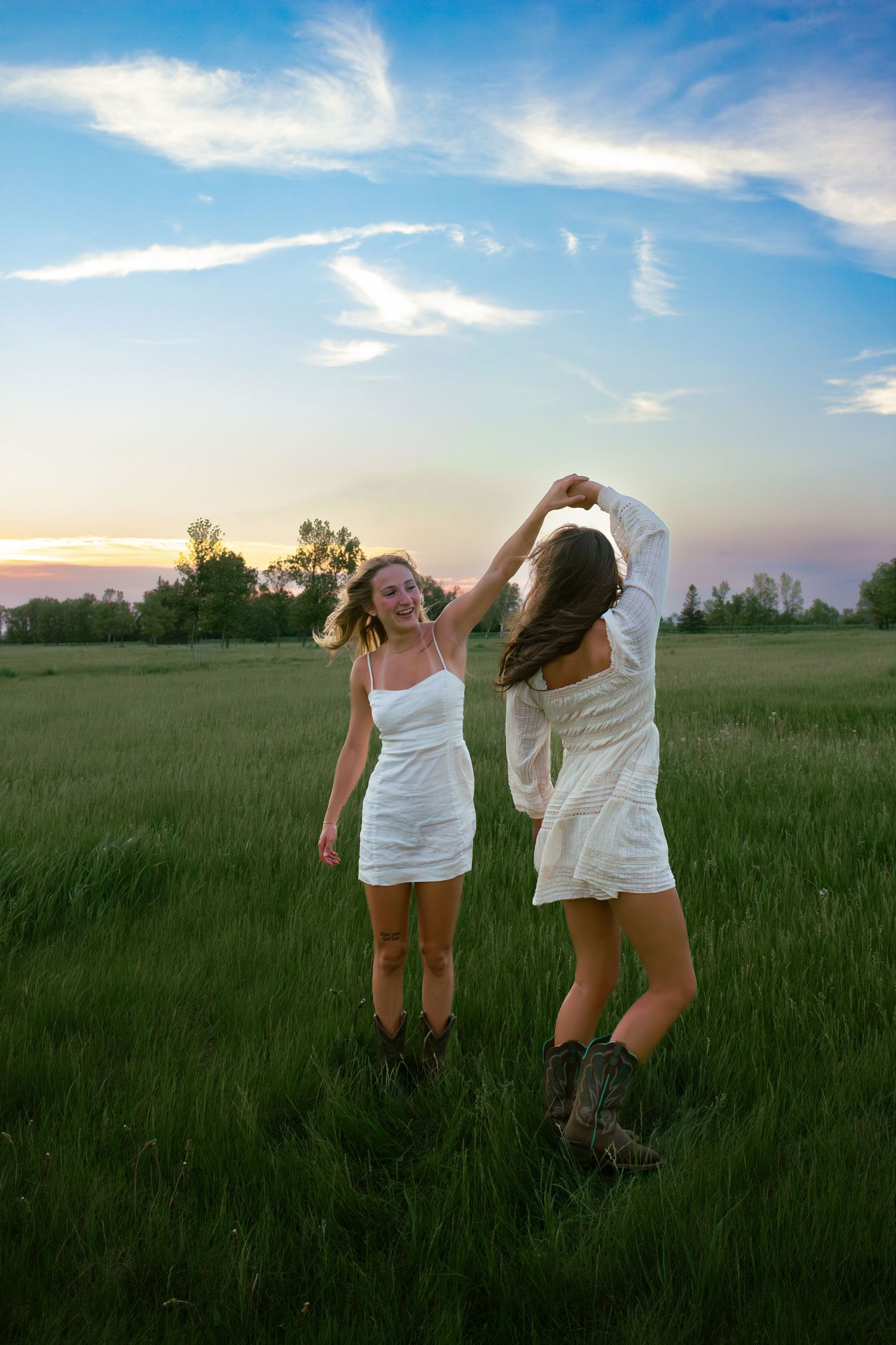 two female friends posing in a field at sunset