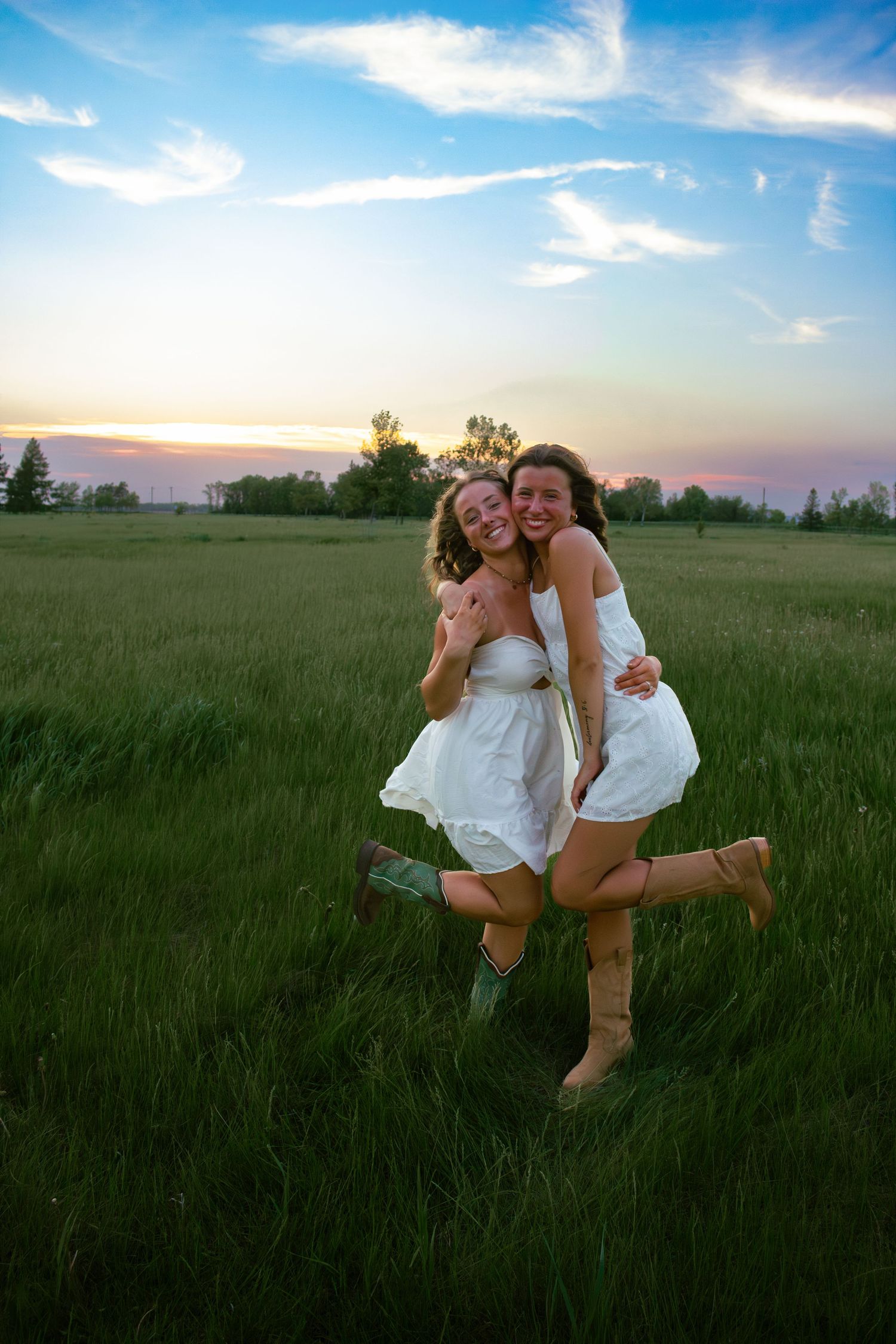 two female friends posing in a field at sunset