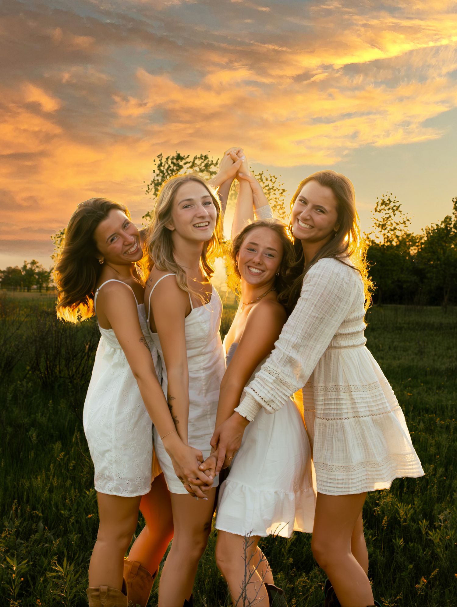 four female friends posing in a field at sunset