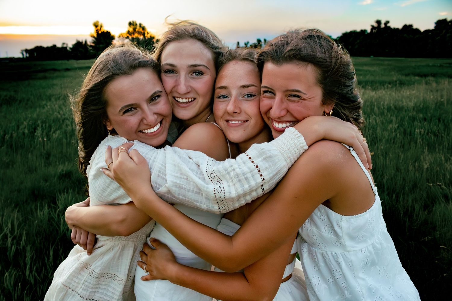 four female friends posing in a field at sunset