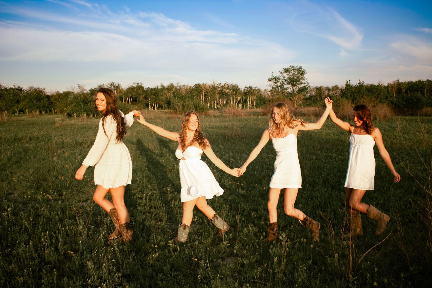 four female friends holding hands waking in a straight line in a field