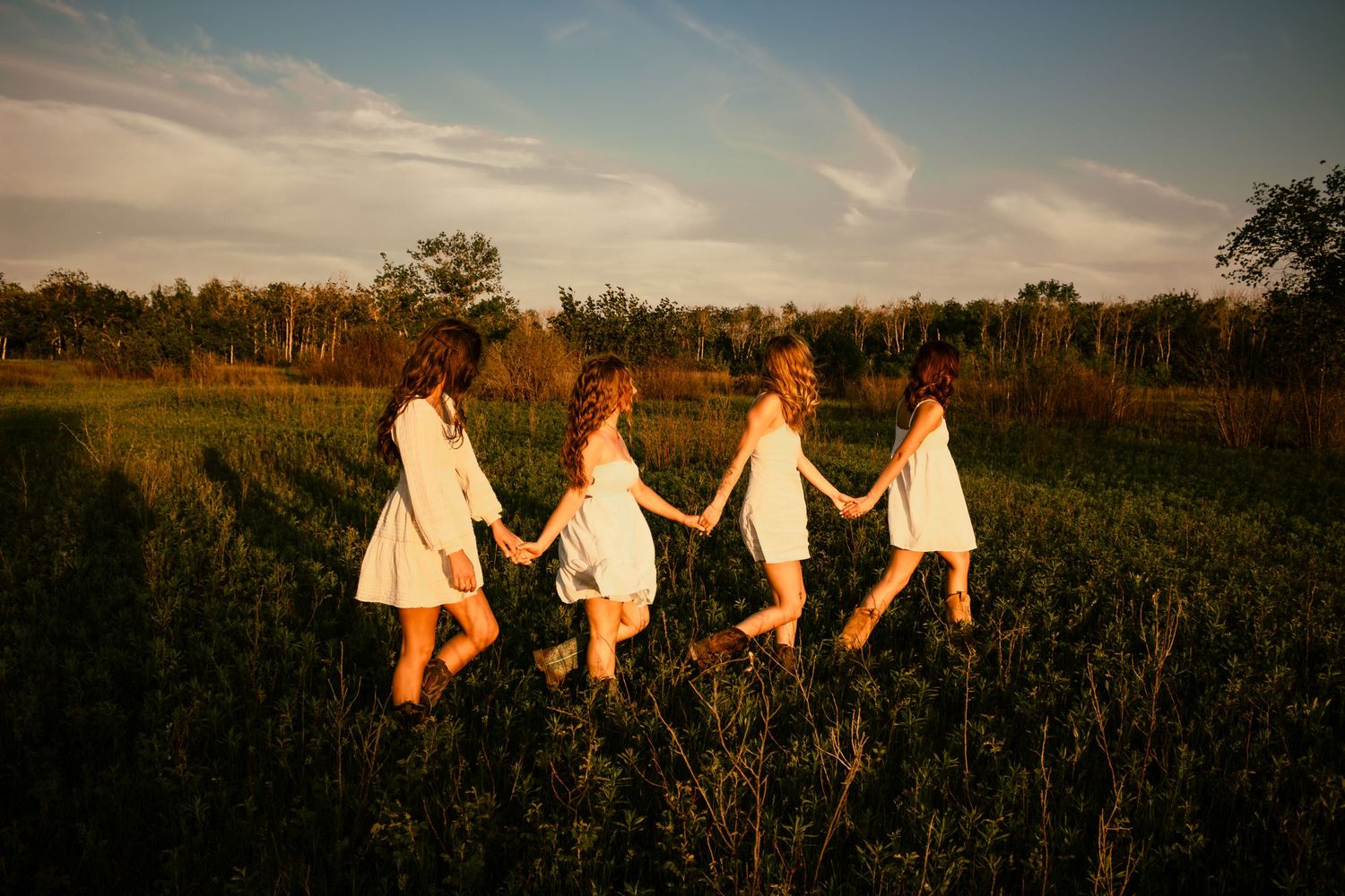 four female friends posing in a field at sunset