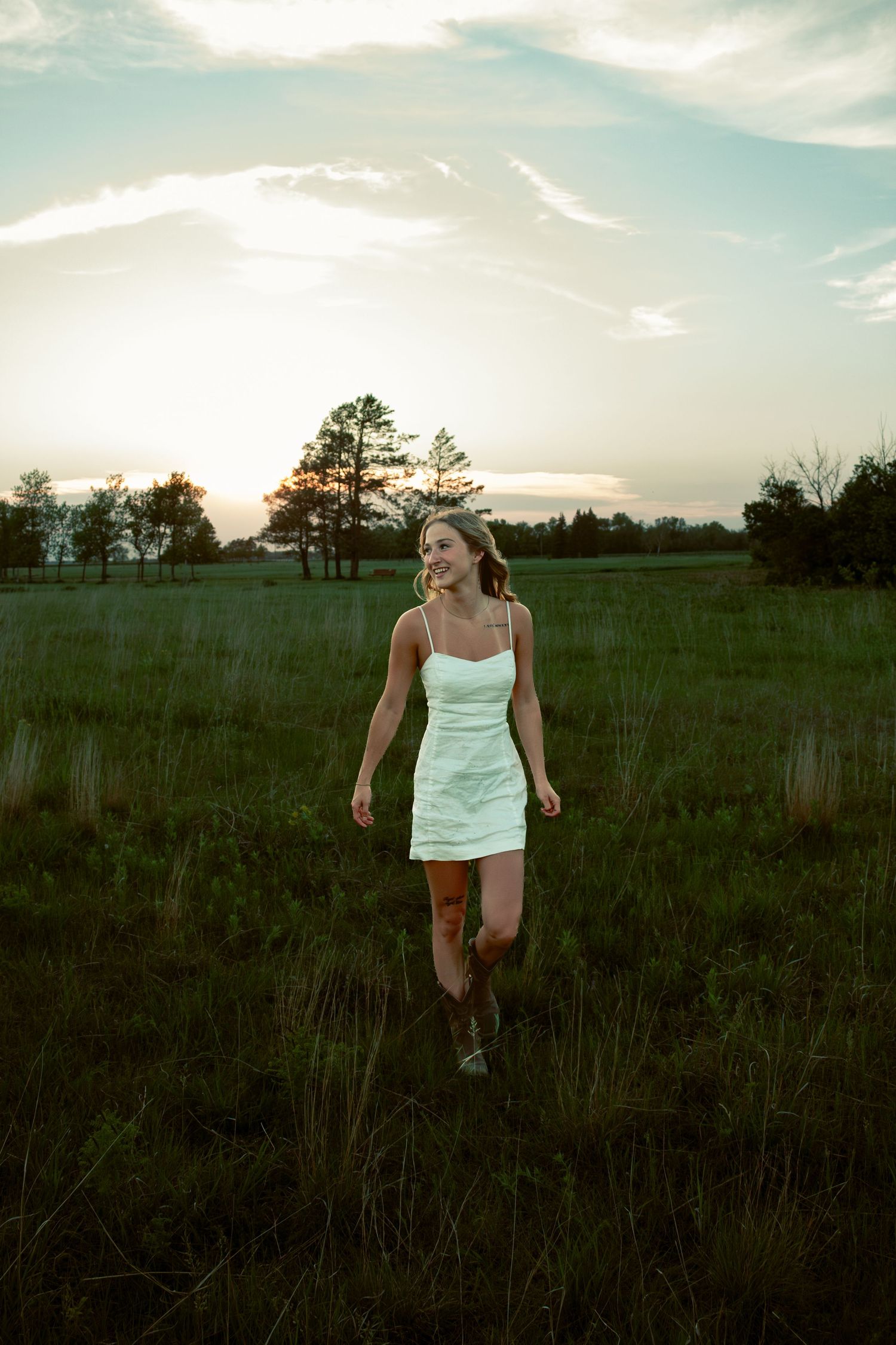 young woman posing in a field at sunset