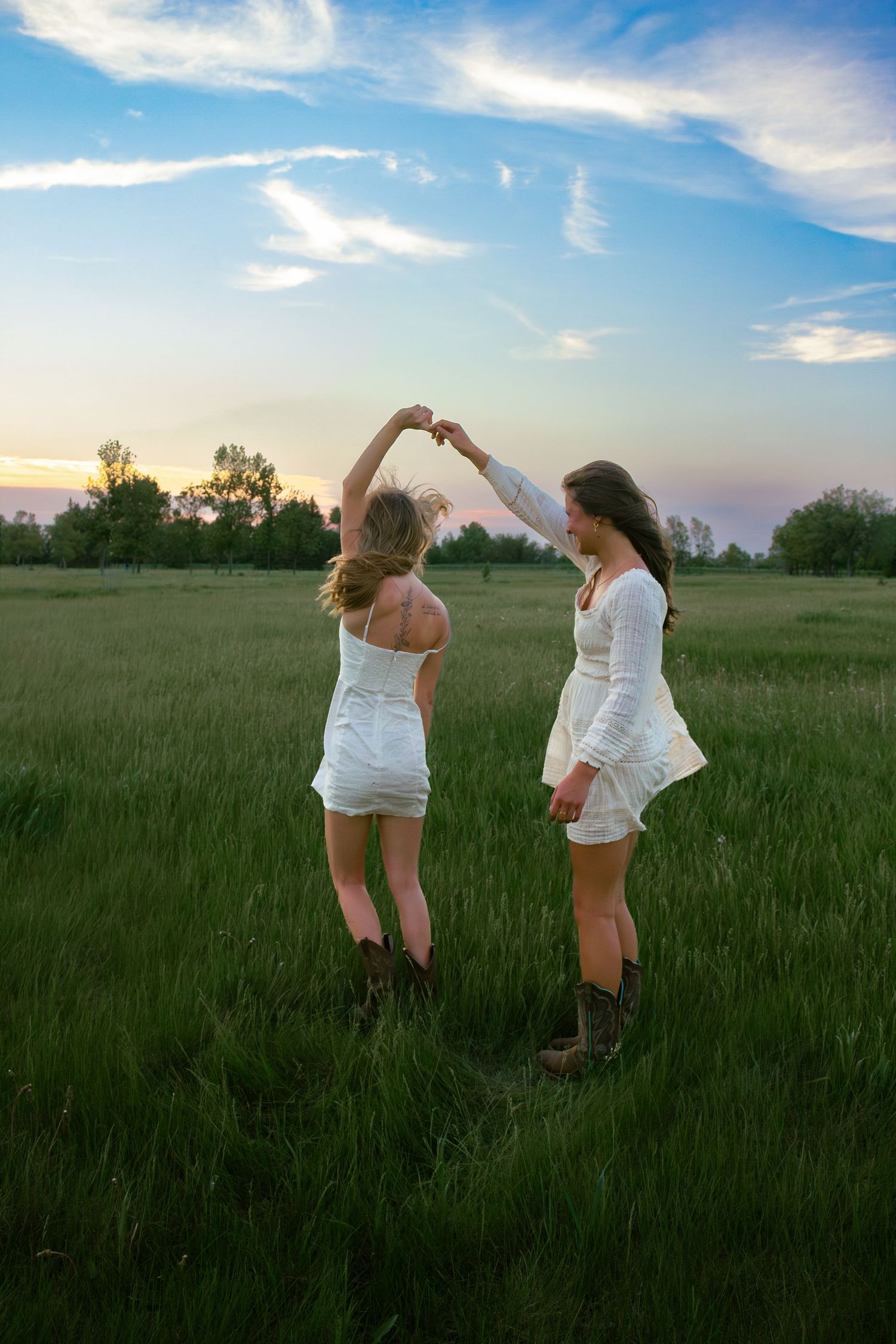 two female friends posing in a field at sunset