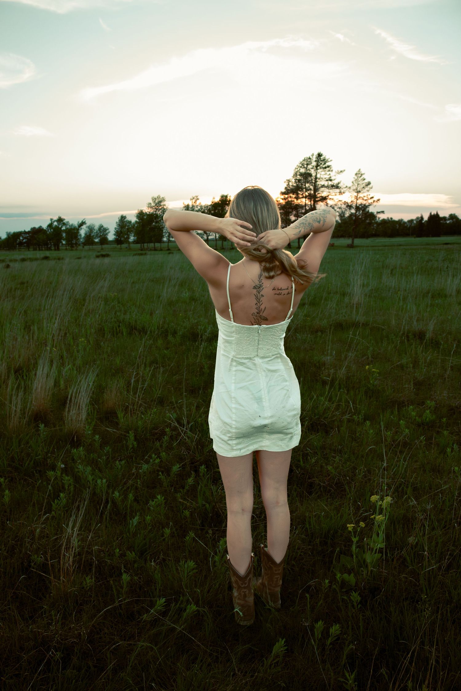 young woman posing in a field at sunset