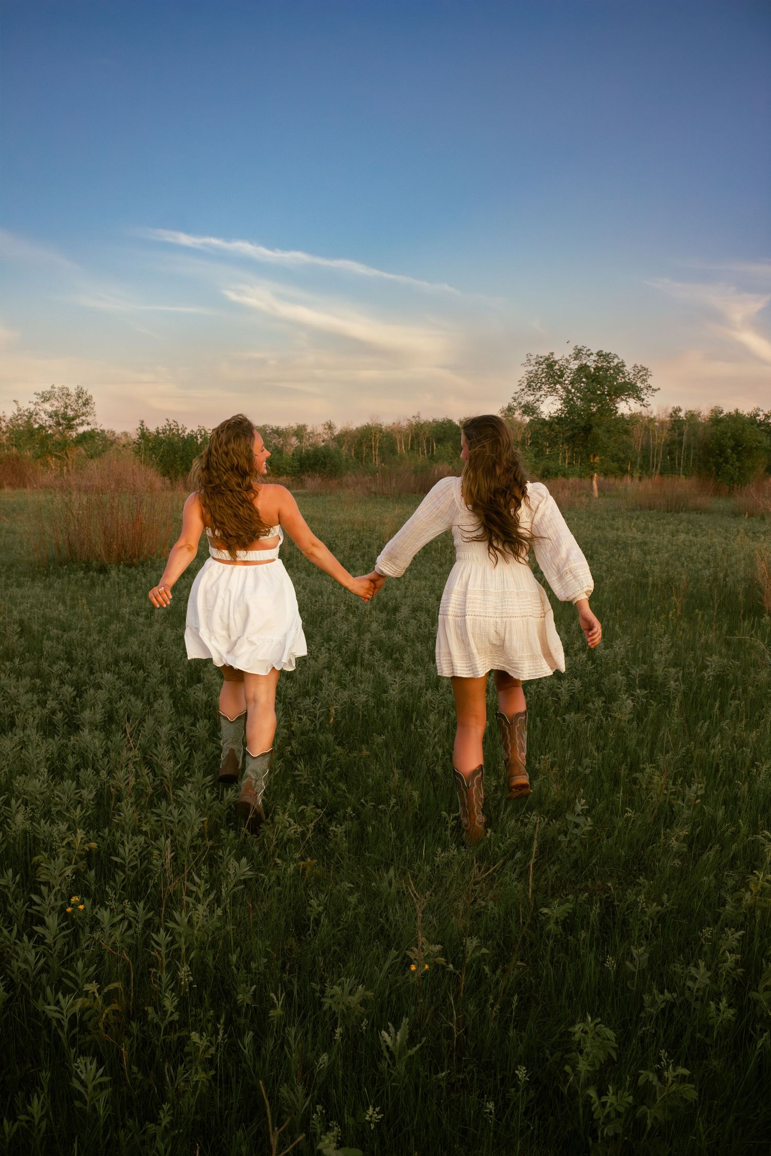 two female friends posing in a field at sunset