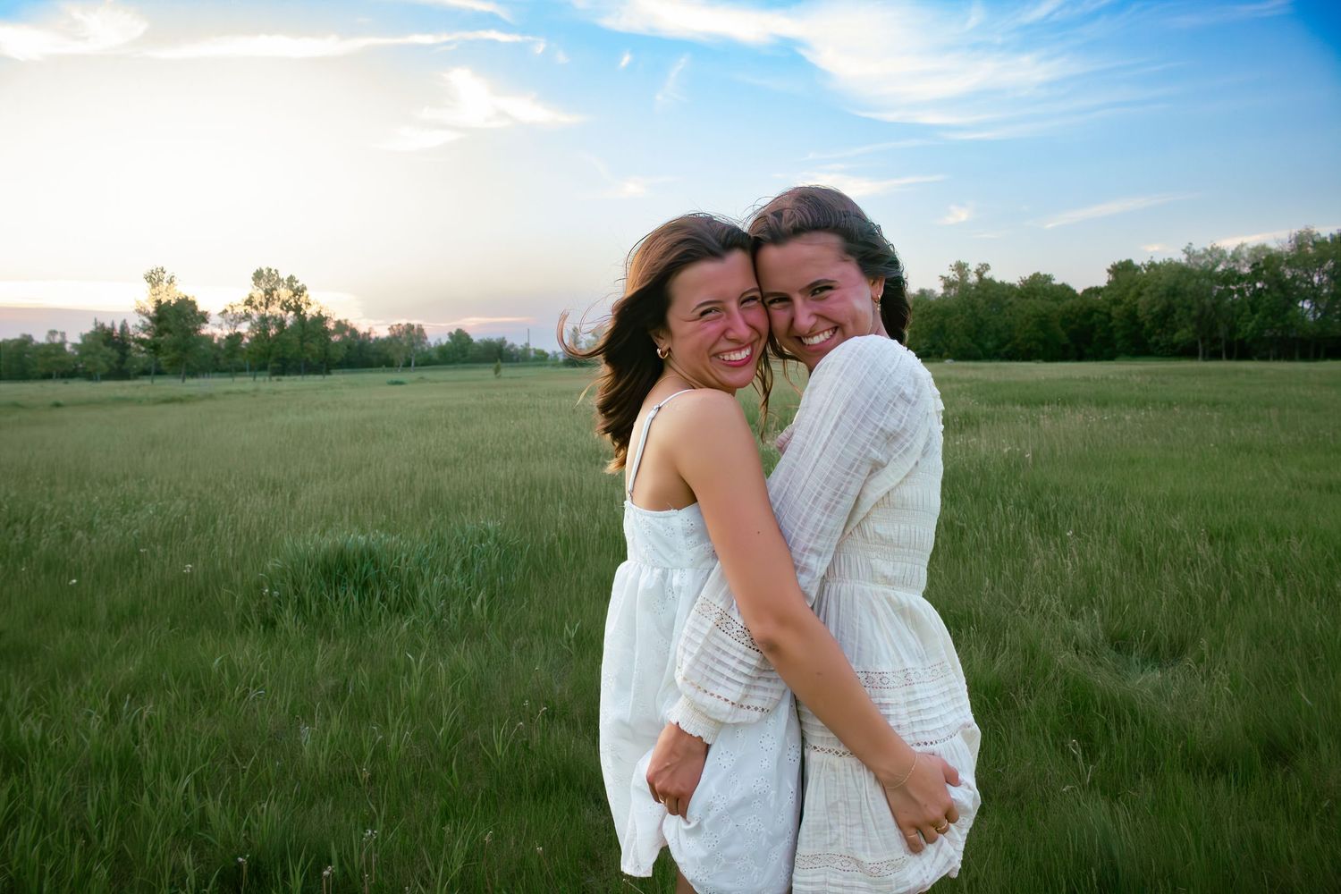 two female friends posing in a field at sunset