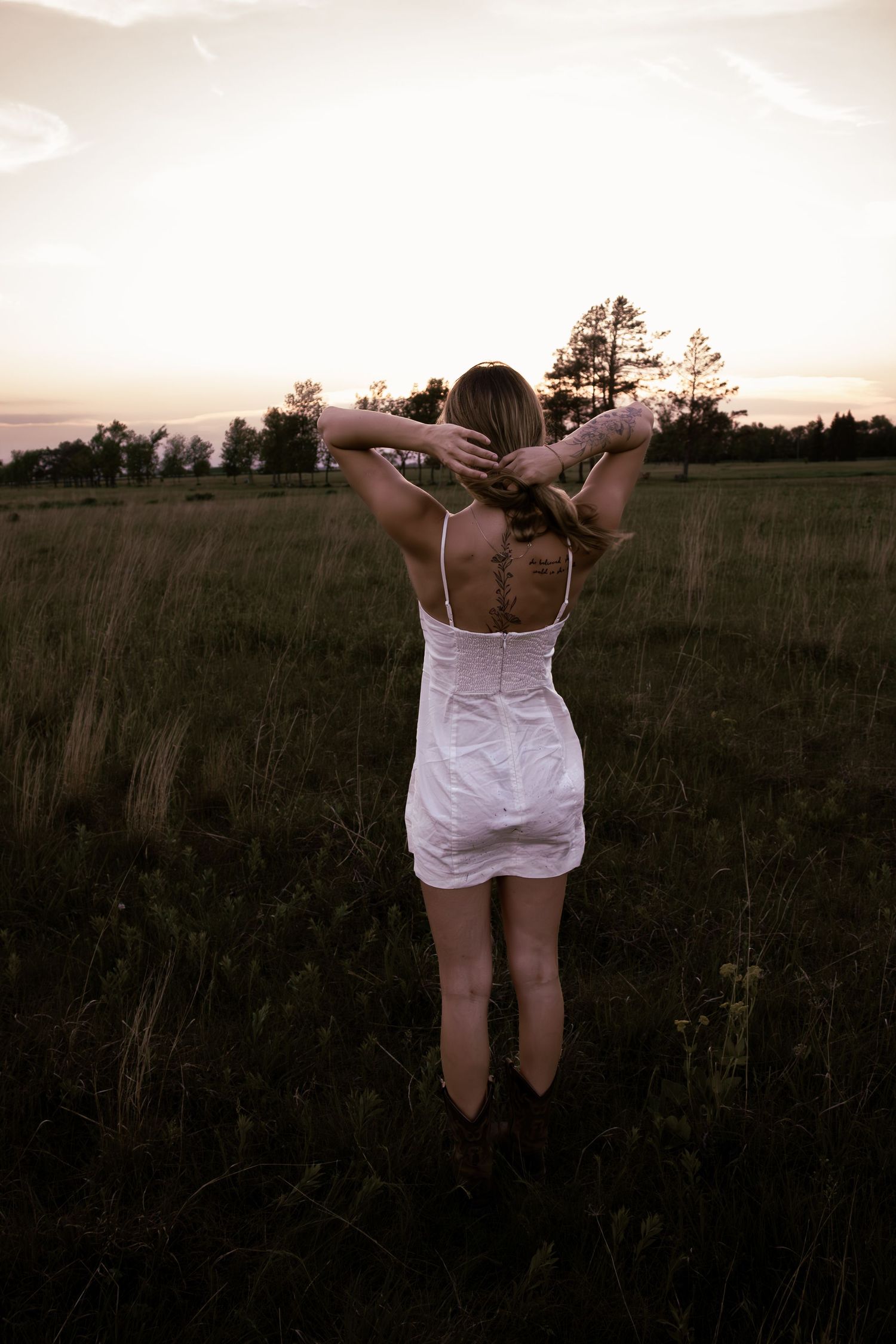 young woman posing in a field at sunset