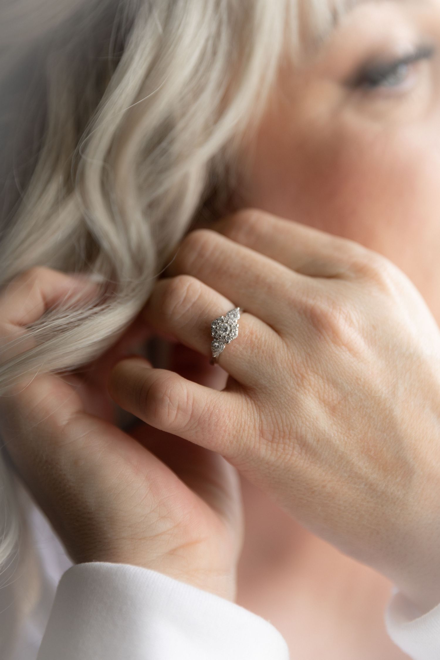A close-up of a diamond ring on a woman's hand touching her silver hair.