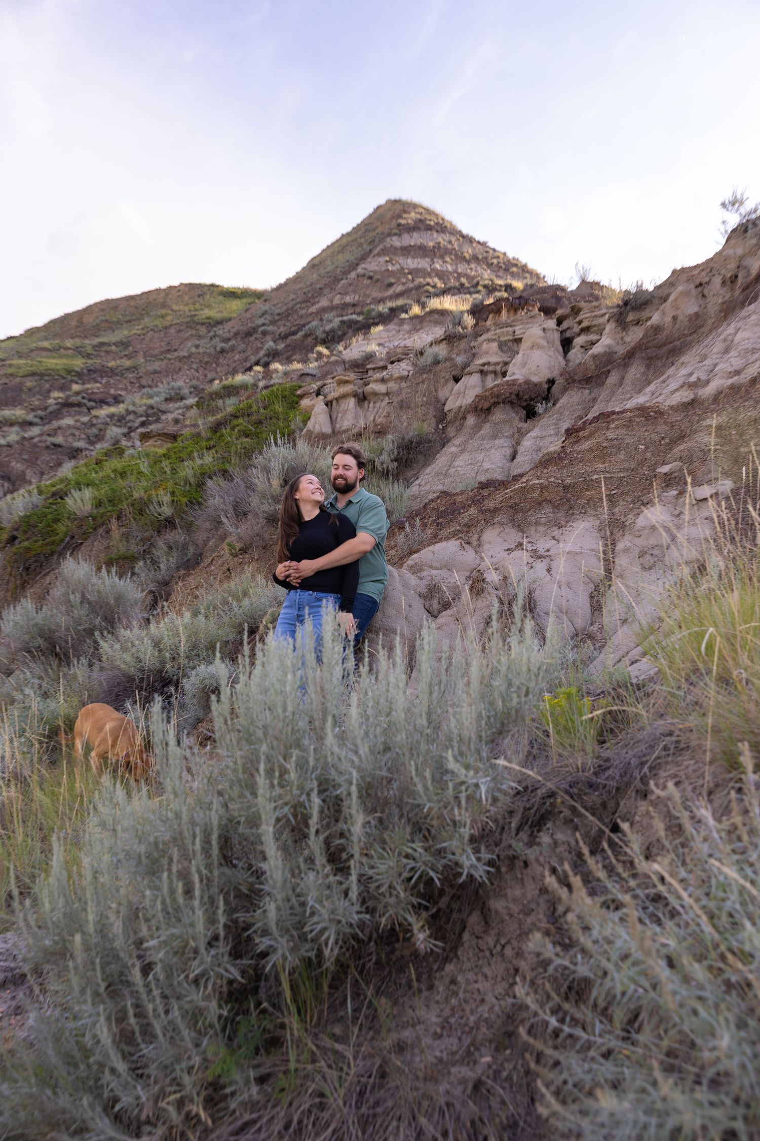 Happy couple embracing on a hillside with dramatic badlands rock formations in the background.