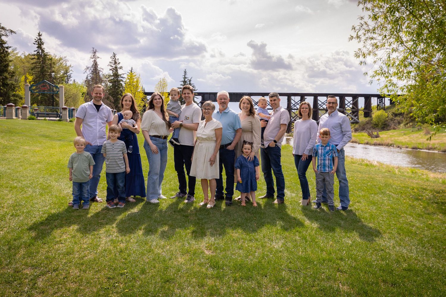Large extended family group portrait on green lawn with a historic trestle bridge in the background.