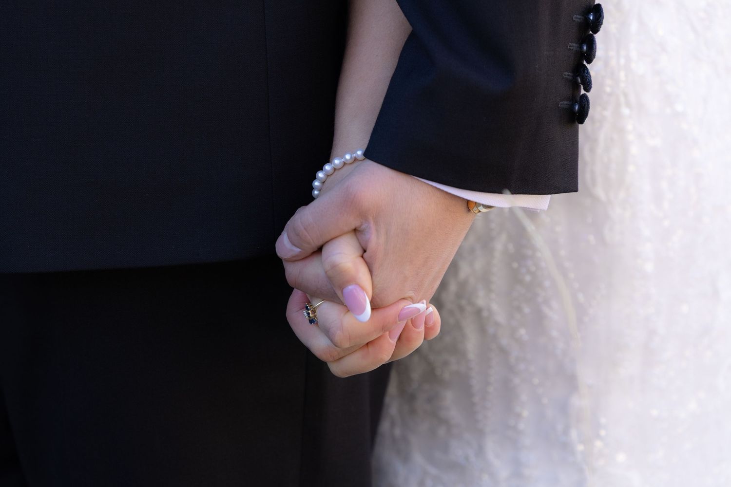 Close-up of bride and groom holding hands showing pearl bracelet and wedding ring at ceremony.