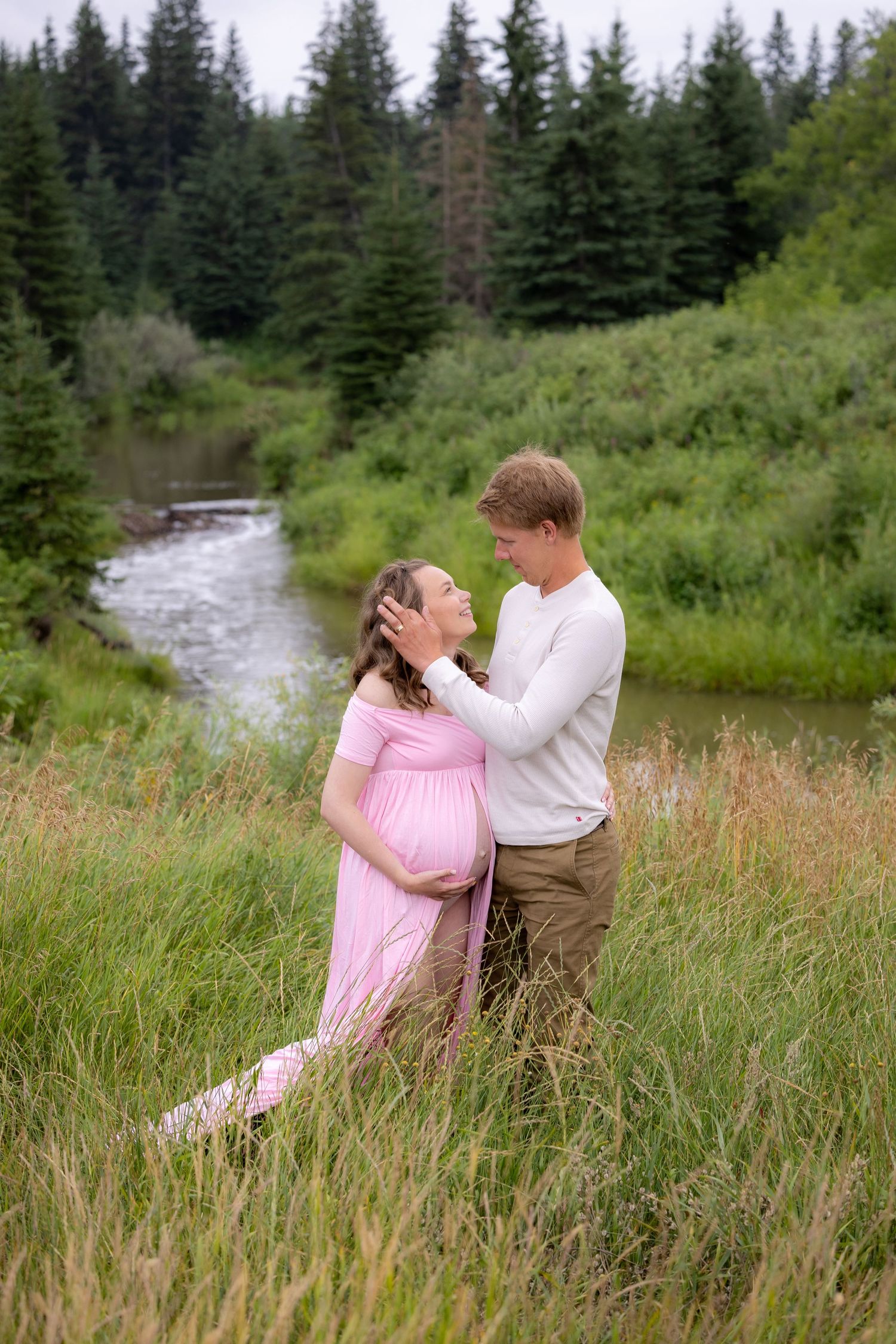Maternity couple embracing in a lush green meadow by a stream.