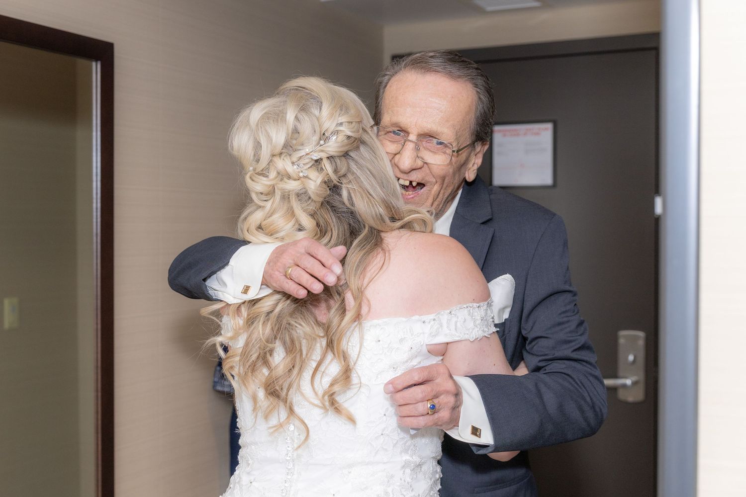 Emotional father hugging his blonde bride daughter in an off-shoulder gown before the wedding ceremony.