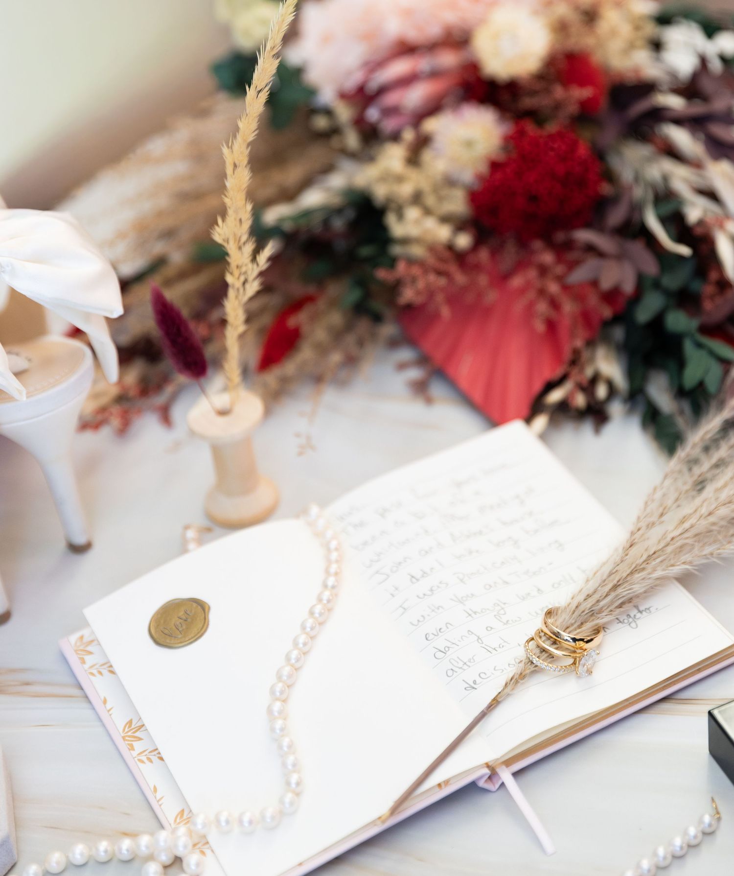 An open wedding guest book with pearls, dried flowers, and bridal shoes nearby.