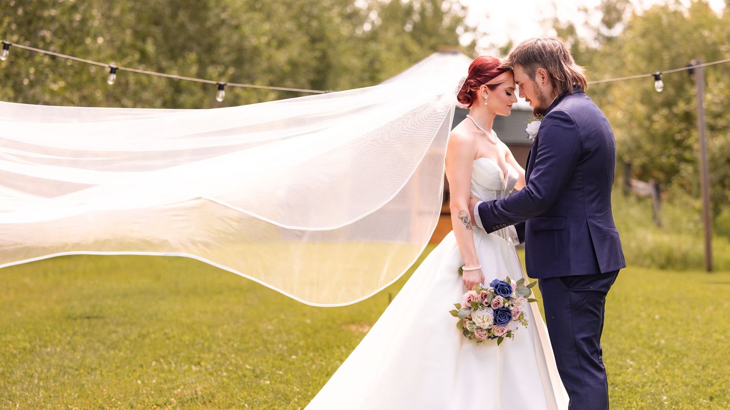 Bride and groom sharing an intimate moment as wedding veil flows in the wind at outdoor ceremony. Central Alberta