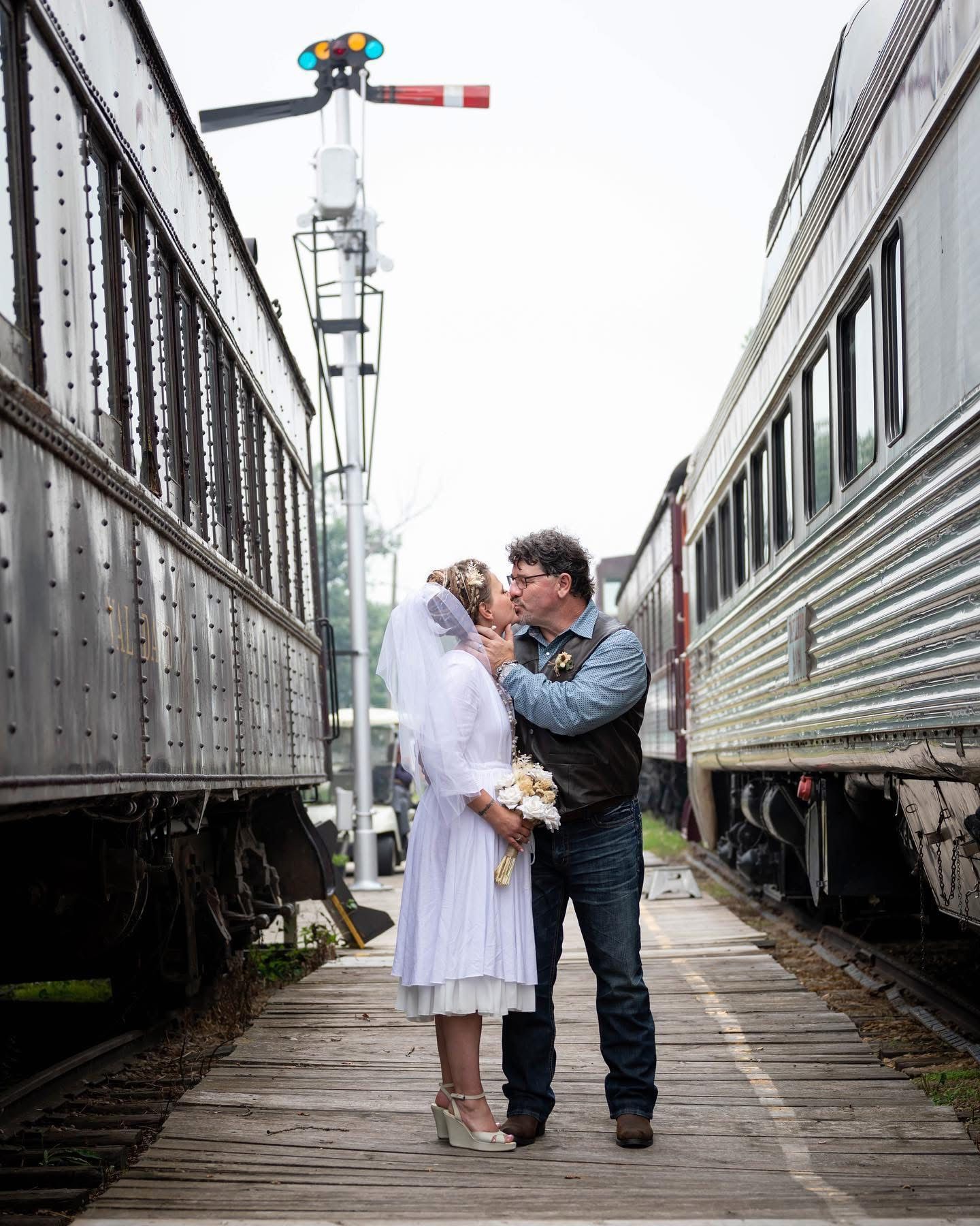 Bride and groom sharing a romantic kiss between vintage train cars on a wooden platform on their wedding day.