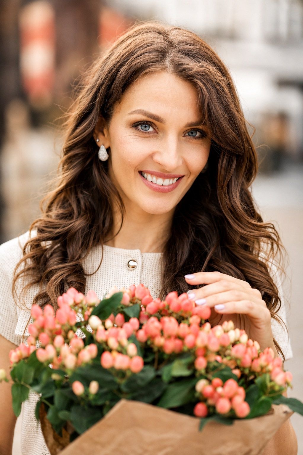 Smiling brunette woman holding a bouquet of pink flowers outdoors.