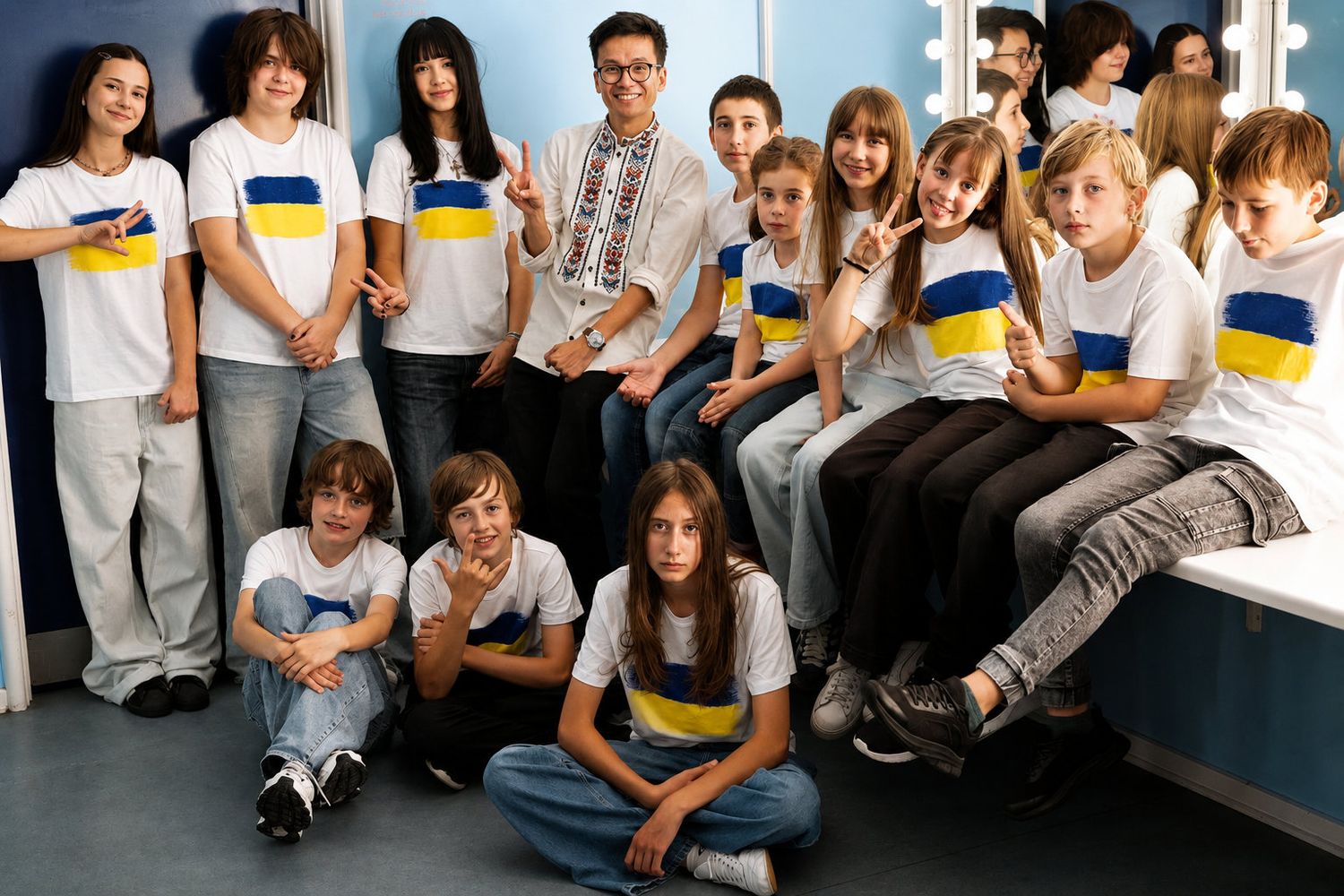 Group of children wearing Ukrainian flag t-shirts posing together in a room, showing peace signs and smiling.