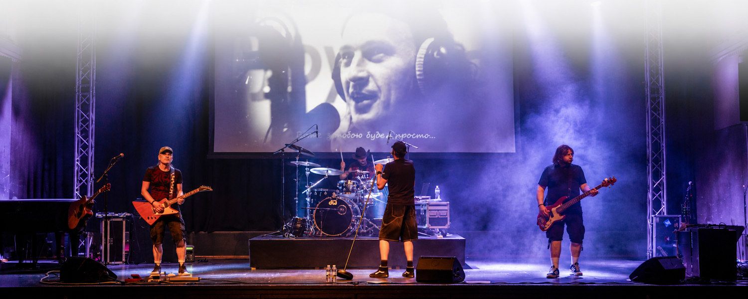Rock band performing on stage with dramatic blue lighting and a large screen backdrop at a live concert.