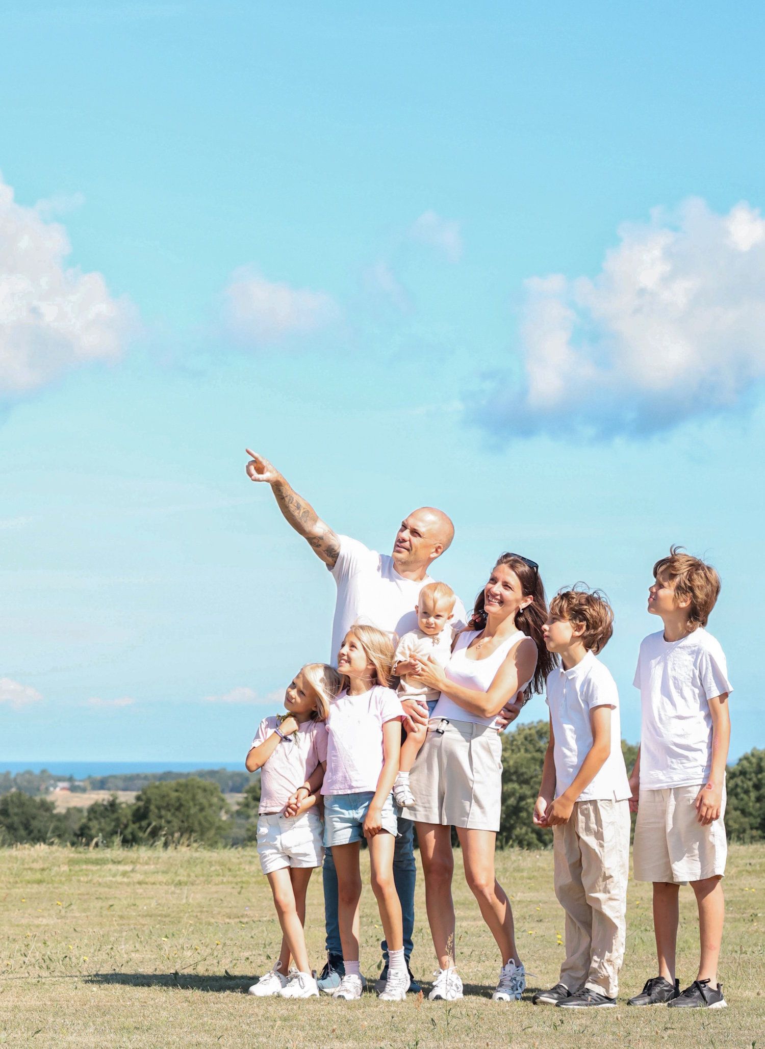Joyful family with kids looking up at blue sky in sunny outdoor field.