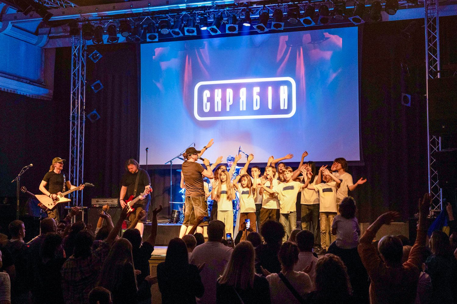 Capario band performs live on stage with guitarist and crowd of fans cheering at an energetic concert event.