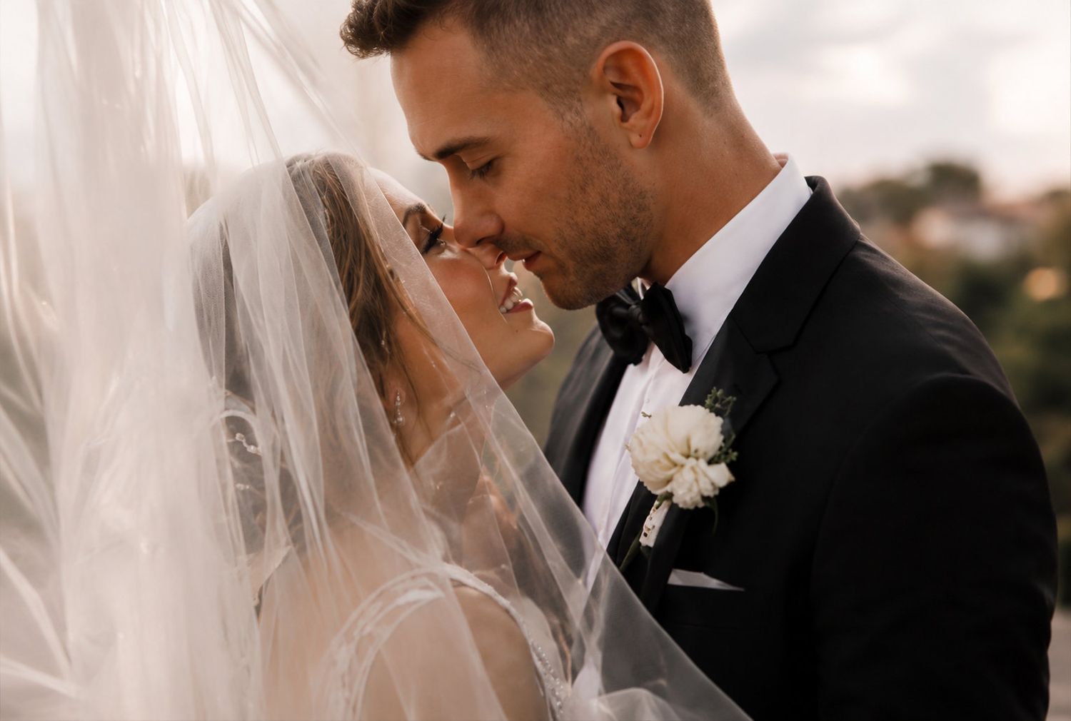 A groom tenderly kisses his bride under a flowing white veil during their romantic outdoor wedding ceremony.