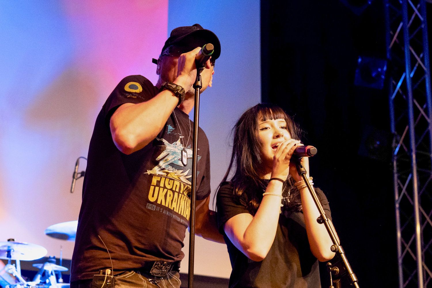 Two singers performing on stage with microphones at a live music event.