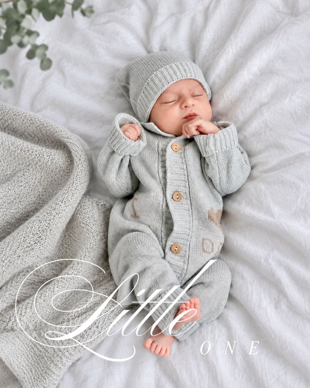 Sleeping newborn baby in gray knit romper and hat on white blanket, Little One text overlay.