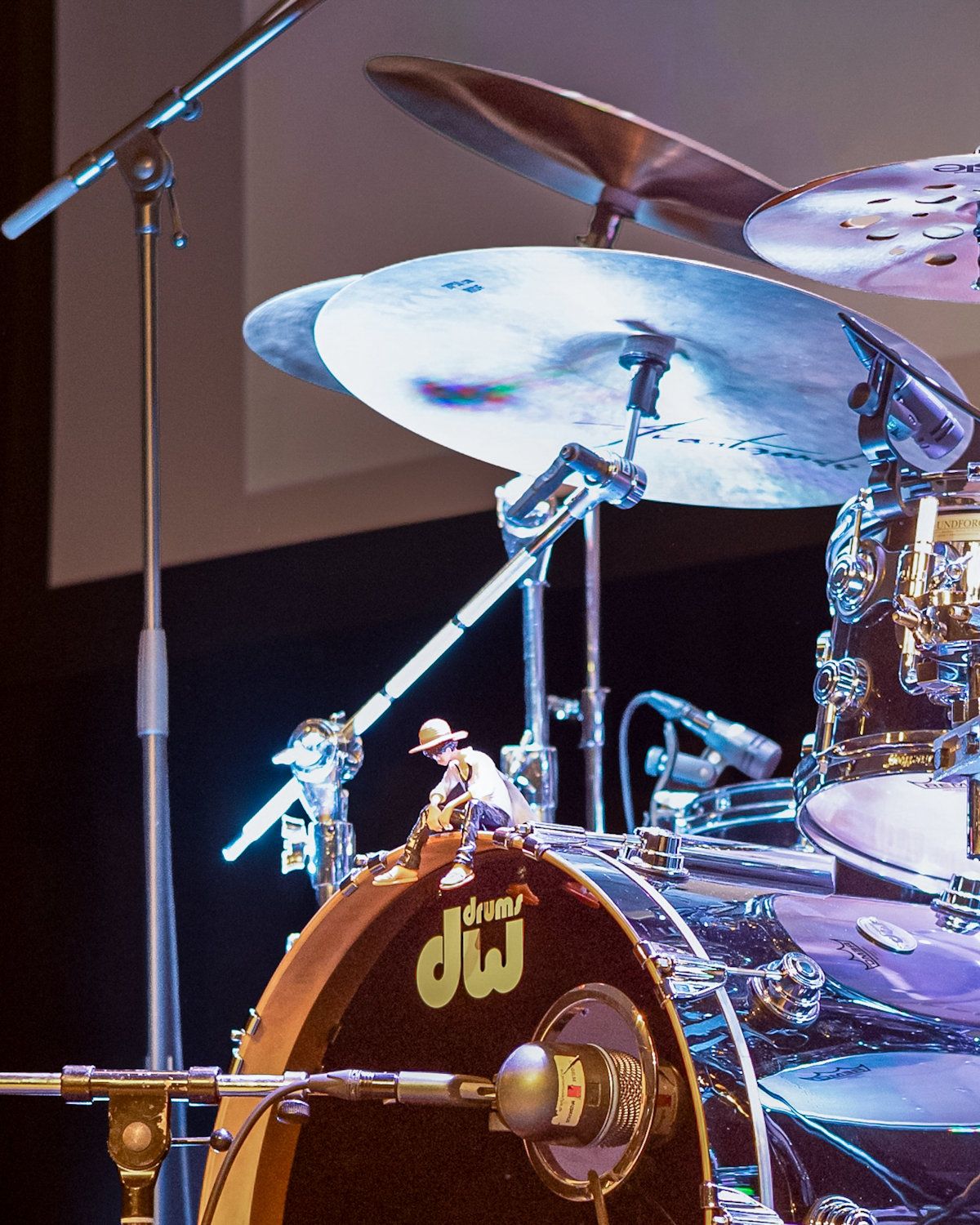 Drummer performing live on stage with DW drum kit, large cymbals, and chrome hardware under blue stage lighting.