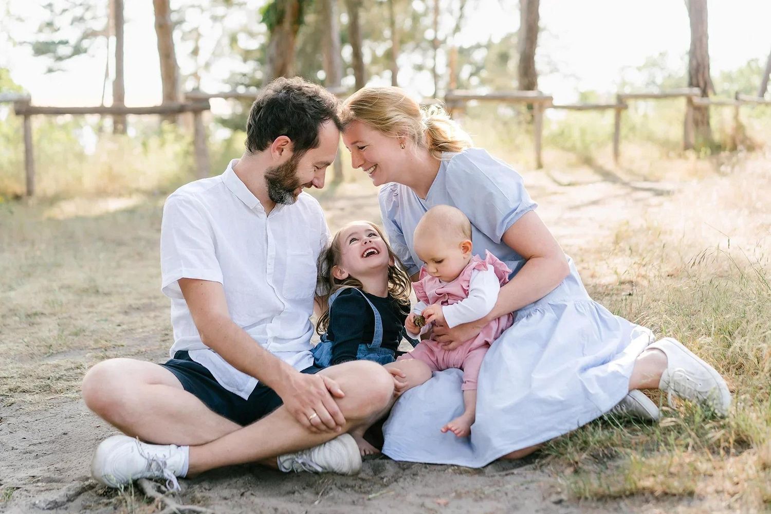 Happy family of four sitting on sandy ground outdoors, laughing and bonding together in nature.