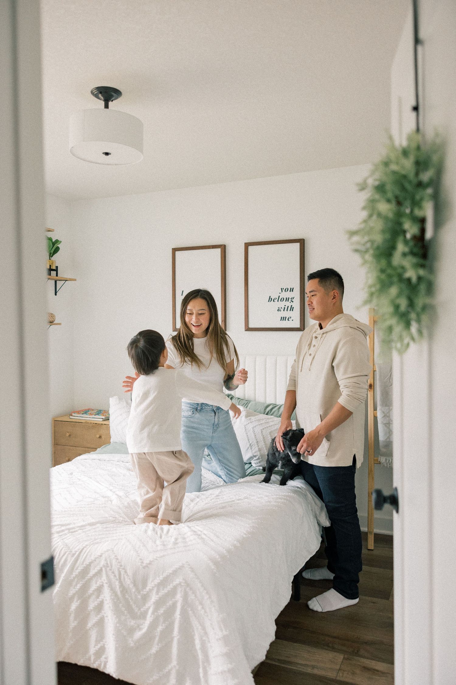 Family spending quality time together in a bright bedroom with white bedding and green plants.