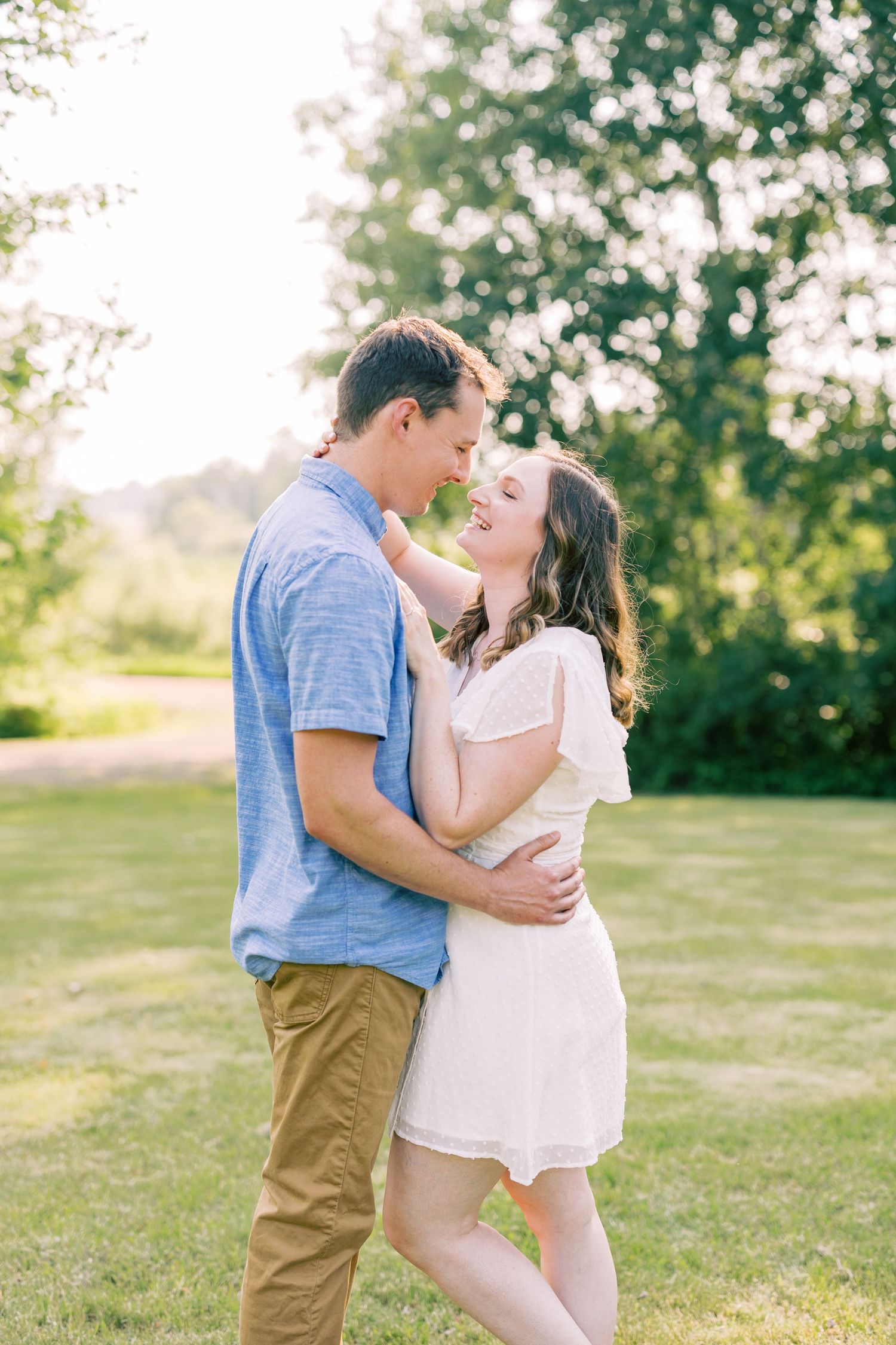 A romantic couple embraces outdoors in a sunlit garden setting with soft bokeh and greenery in the background.