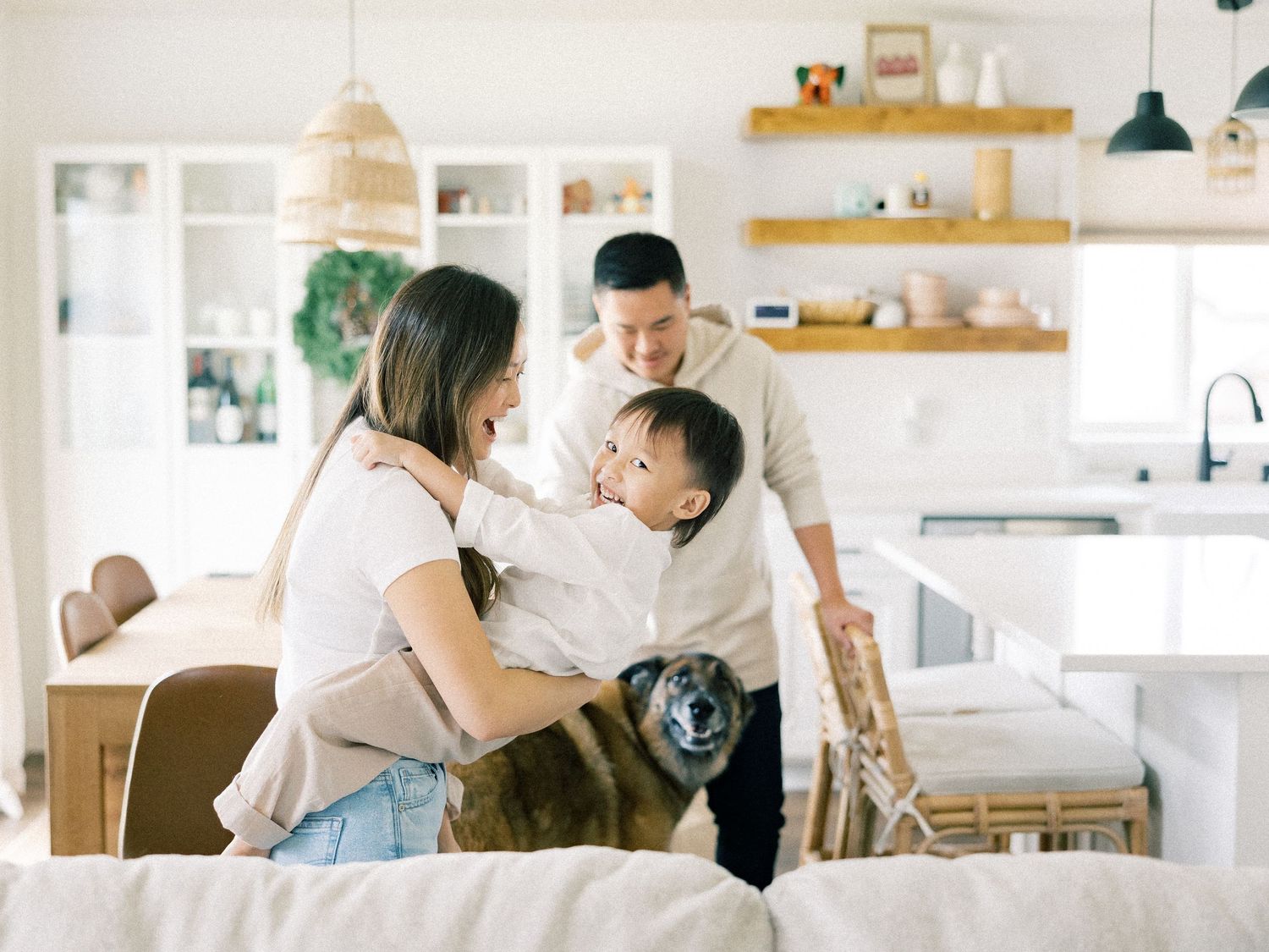 A loving family shares a joyful moment together in their bright modern white kitchen with wooden shelving.