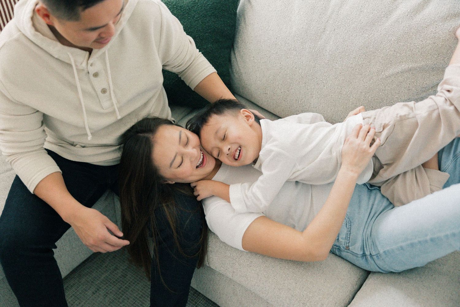 Family relaxes together on a comfortable gray couch at home during quiet moment.