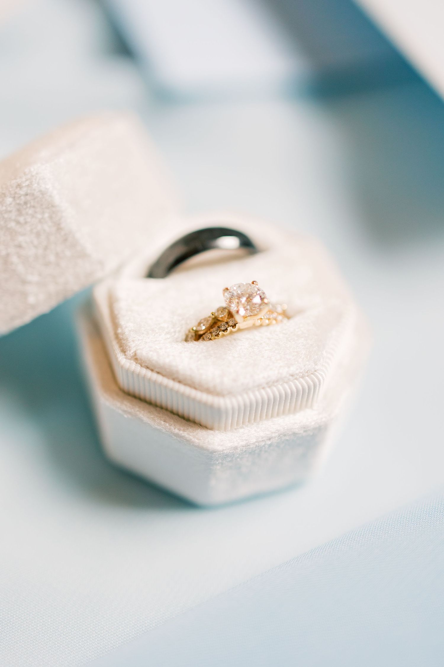 A delicate diamond engagement ring nestled in a cream-colored hexagonal ring box on a soft blue surface.