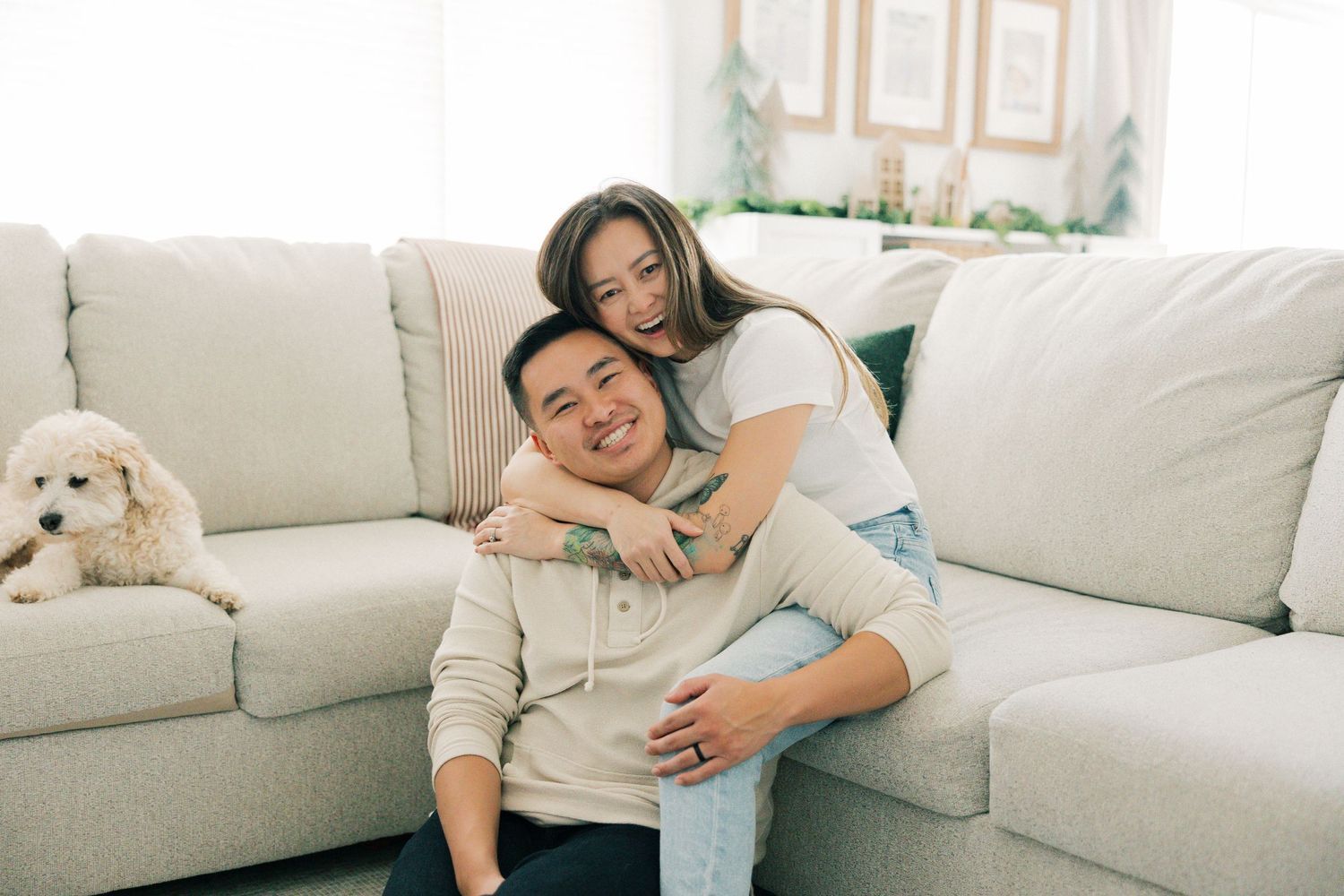 A happy couple embraces while relaxing on a light gray sectional sofa with a plush stuffed animal nearby.