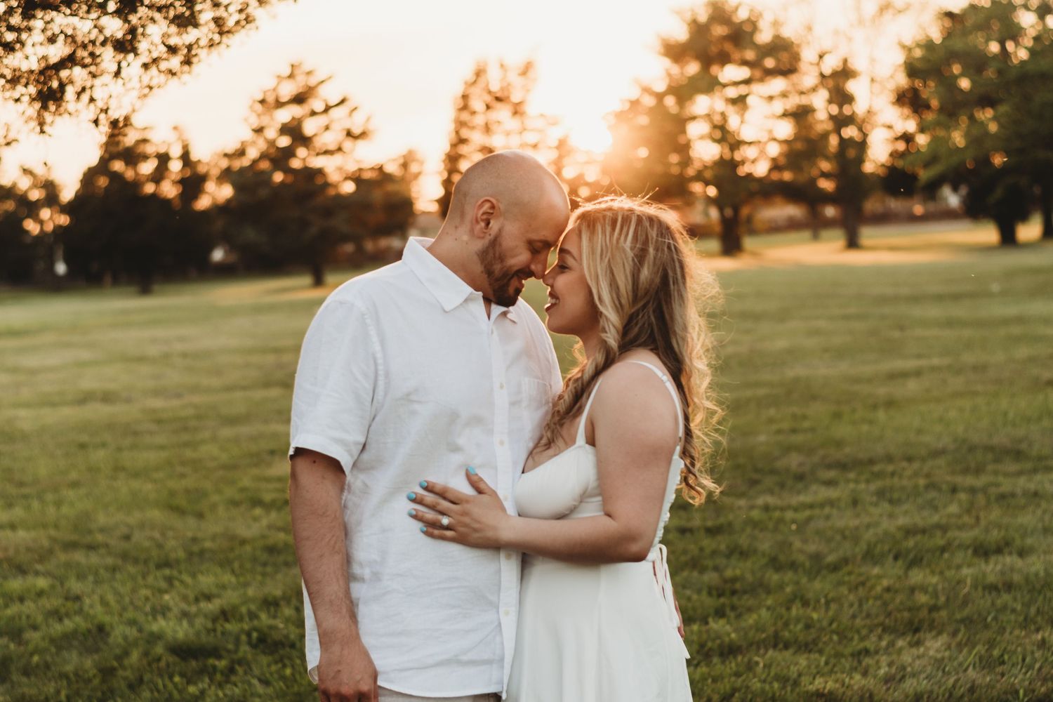 A couple shares a romantic moment at golden sunset in a lush green park setting.